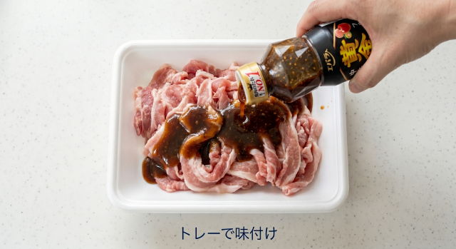 豚肉トレーパックの上で豚こま肉に直接焼肉のたれをかける様子
